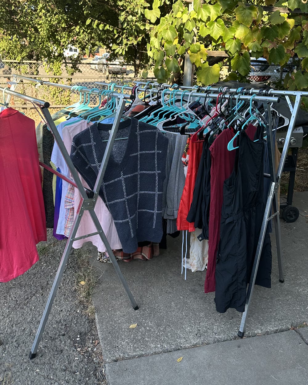 A rack of sorted clothing standing on the driveway in evening light, every piece on a teal hanger.